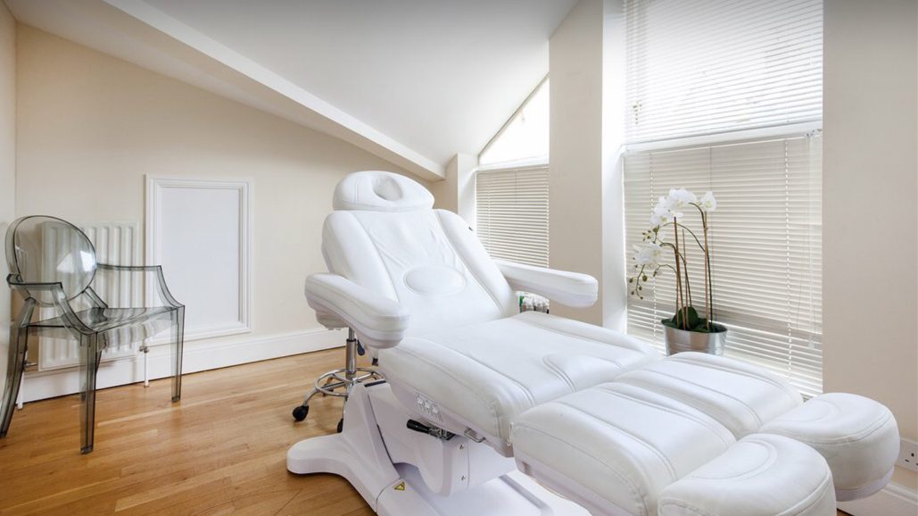 An upstairs treatment room with a white couch, wooden floor, shuttered windows and an orchid on the sill.